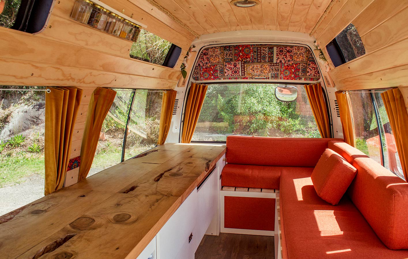 Komfortabel eingerichtetes Wohnmobil mit Holzverkleidungen, warmen Farbtönen und gemütlicher Sitzgelegenheit, ideal für den DIY-Innenausbau.